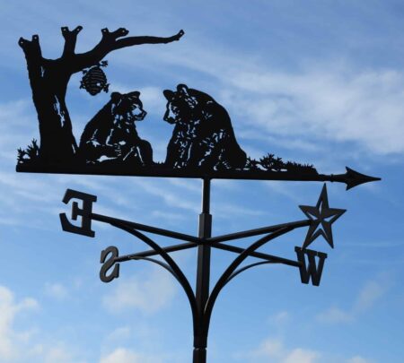 Grizzly bears and honey Bees on top of a black Weathervane against a blue sky