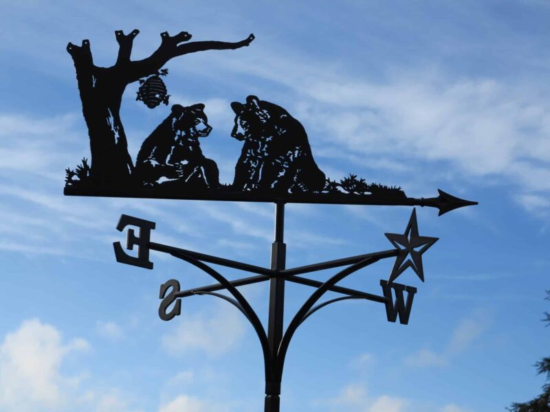 Grizzly bears and honey Bees on top of a black Weathervane against a blue sky