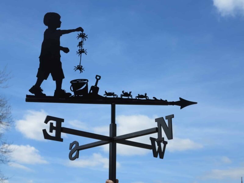 a weathervane design of a child crabbing at the seaside against a light blue sky