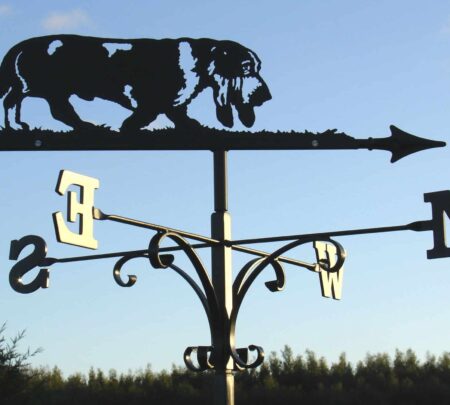 a black Basset Hound Dog Weathervane against a blue sky and hedge row