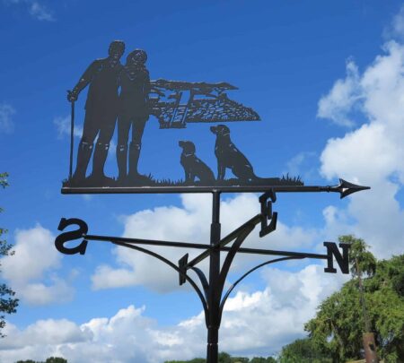 a dog walker themed weathervane - picturing a Couple Walking, Hills And Dogs against a blue sky